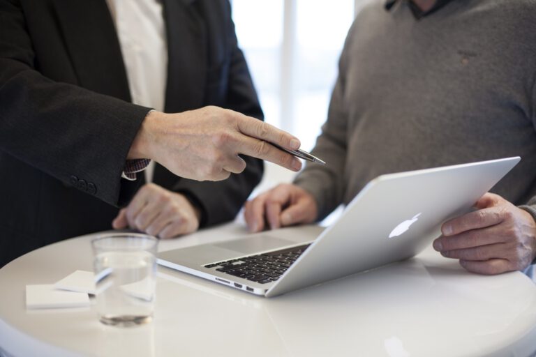 Zwei Menschen stehen an einem Macbook und unterhalten sich